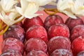 Red plums on an orange background, accompanied by a bouquet of white flowers and green lentils.