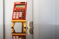 Red pocket calculator on easel with Stack of coins