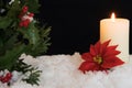 Red Poinsettia flower with lit candle and Mistletoe in snow. Christmas Background with holiday theme Royalty Free Stock Photo
