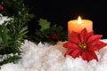 Red Poinsettia flower with lit candle and Mistletoe in snow. Christmas Background with holiday theme Royalty Free Stock Photo