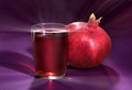 Red pomegranate, and glass of garnet juice on a violet background, with solar patches of light Royalty Free Stock Photo