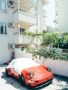 Red Porsche 911 Carrera stands covered with a cloth near an apartment building Royalty Free Stock Photo