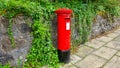 Red Post Office pillar box in front of stone wall covered in ivy.