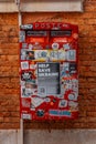 Red postbox adorned with stickers and Help Save Ukraine message flyer against red brick wall