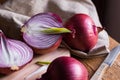 Red or purple onion cut in half, green germs, wood breadboard, linen towel, knife, kitchen table by window