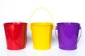 Three metal buckets colored red, yellow, and purple standing in row against solid white background Royalty Free Stock Photo