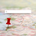 A red pushpin is placed on a detailed map. The background features a blurred search bar Royalty Free Stock Photo