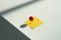 Red pushpin securing a yellow sticky note on a white surface Royalty Free Stock Photo