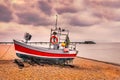 Red quaint, traditional fishing boat moored on the pebble shingle beach in Deal, Kent, UK with the pier in the background