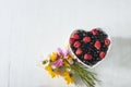 Red raspberries and red currants in the white bowl shape heart and bouquet of wild flowers Royalty Free Stock Photo