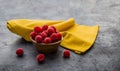 Red raspberries placed in a round wooden bowl accompanied by a yellow napkin, all on a gray background Royalty Free Stock Photo