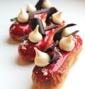 Red raspberry eclairs with meringues and chocolate decorations on light background
