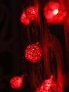 Red Rattan ball garland on patterned wall. Christmas led lights on dark background. Blurred glowing light bulb garland. Closeup Royalty Free Stock Photo