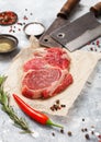 Red raw beef rib eye steak fillet with steel hatchets on light background with salt and pepper