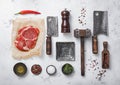 Red raw rib eye steak with meat cleavers,tenderizer,fork,knife and other kitchen meat utensils with oil,herbs,salt and pepper on Royalty Free Stock Photo