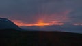 Red rays of the midnight sun through the clouds over the mountains