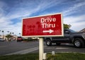 Red rectangular sign reading Drive Thru for fast food restaurant with car passing against blue sky and clouds