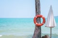 Red rescue lifebuoy hangs on a tree in front of open sea, close to closed umbrella. Tropical destination, Thailand Royalty Free Stock Photo