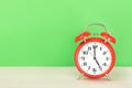 Red retro alarm clock with five o`clock, on wooden table on a green background Royalty Free Stock Photo