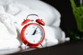 Red retro alarm clock near nightstand at bed with white blanket sheet at home in hotel bedroom. morning time to wake up early rise