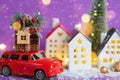 Red retro car on snow carries gift box with home key with keychain cottage on roof past houses with fairy lights, Christmas tree. Royalty Free Stock Photo