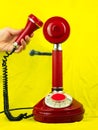 Red retro phone in female hand on yellow background. Vintage telephone device on modern pastel color surface. Nostalgia Royalty Free Stock Photo