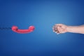 A red retro phone receiver hangs opposite to an empty male hand on a blue background. Royalty Free Stock Photo