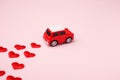 Red retro toy red car with red bow for Valentine`s day on pink background with heart confetti Royalty Free Stock Photo
