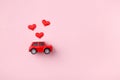 Red retro toy red car with red bow for Valentine`s day on pink background with heart confetti. Top view, flat lay Royalty Free Stock Photo