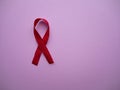 Red ribbon as the universal symbol of awareness and support for people living with AIDS and HIV on a pink background with copy sp