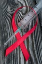 Red Ribbon Symbol for World AIDS Day. On top of it lies a medical syringe. Lies on black pine boards