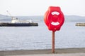 Red ring for water safety at sea dock and ships in background