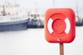 Red ring for water safety at sea dock and ships in background