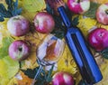 Red and ripe apples in a wicker basket with maple leaves.A bottle of wine and a thin-stemmed glass