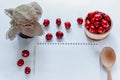 Red ripe cherries with jam jar, wooden spoon and notebook on white background. Flat lay. Food concept. Royalty Free Stock Photo