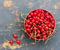 Red ripe cherries with tails in a circular plate on an old black wooden background with a crack Royalty Free Stock Photo