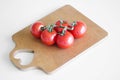 Cherry tomatoes on a branch lie on a wooden cutting board on a white table. The heart is cut out on the board. Royalty Free Stock Photo