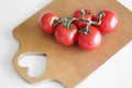 Cherry tomatoes on a branch lie on a wooden cutting board on a white table. The heart is cut out on the board. Royalty Free Stock Photo