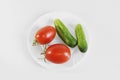 Red ripe juicy tomatoes and green cucumber on a white plate. Light gray background Royalty Free Stock Photo