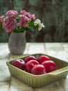 Red ripe plums lie in a deep square ceramic olive plate on a light wooden table. In the background, a small bouquet of Royalty Free Stock Photo