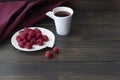 red ripe raspberries are on a white plate, next to them there is a cup of vitamin tea and red textile on wooden background, copysp Royalty Free Stock Photo