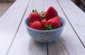 Red ripe strawberries in a light blue bowl on white wooden rustic table