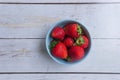 Red ripe strawberries in a light blue bowl on white wooden rustic table