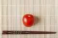 Red ripe tomato and chopsticks on bamboo mat closeup. Natural vegetables for dietary and healthy food. Chinese or japanese kitchen Royalty Free Stock Photo