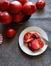 Red ripe tomatoes with water droplets  in a black bowl and sliced tomato on white plate. Royalty Free Stock Photo