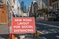 A red roadwork sign next to a bus lane saying new road layout for social distancing on an empty street in London, with St Pauls in