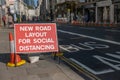 A red roadwork sign next to a bus lane saying new road layout for social distancing with a London street in the background