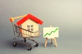 A red roof house in a trading cart and green arrow up on a stand. Increasing the cost and liquidity of real estate. Attractive Royalty Free Stock Photo