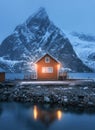 Red rorbu on sea coast and snow covered mountain at night