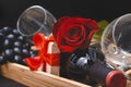 Red rose, bottle of wine, 2 glasses, dark grapes, corkscrew, gift box with ribbon on black background Royalty Free Stock Photo
